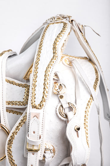 MONTURA COLA DE PATO CON CANTINA DE PIEL DE AVESTRUZ BLANCA GUARDAS TRENZADAS DORADAS FUSTE Y HERRAJE DE ACERO MONEL FONDO BLANCO CON PEDRERIA DE ZIRCONIA